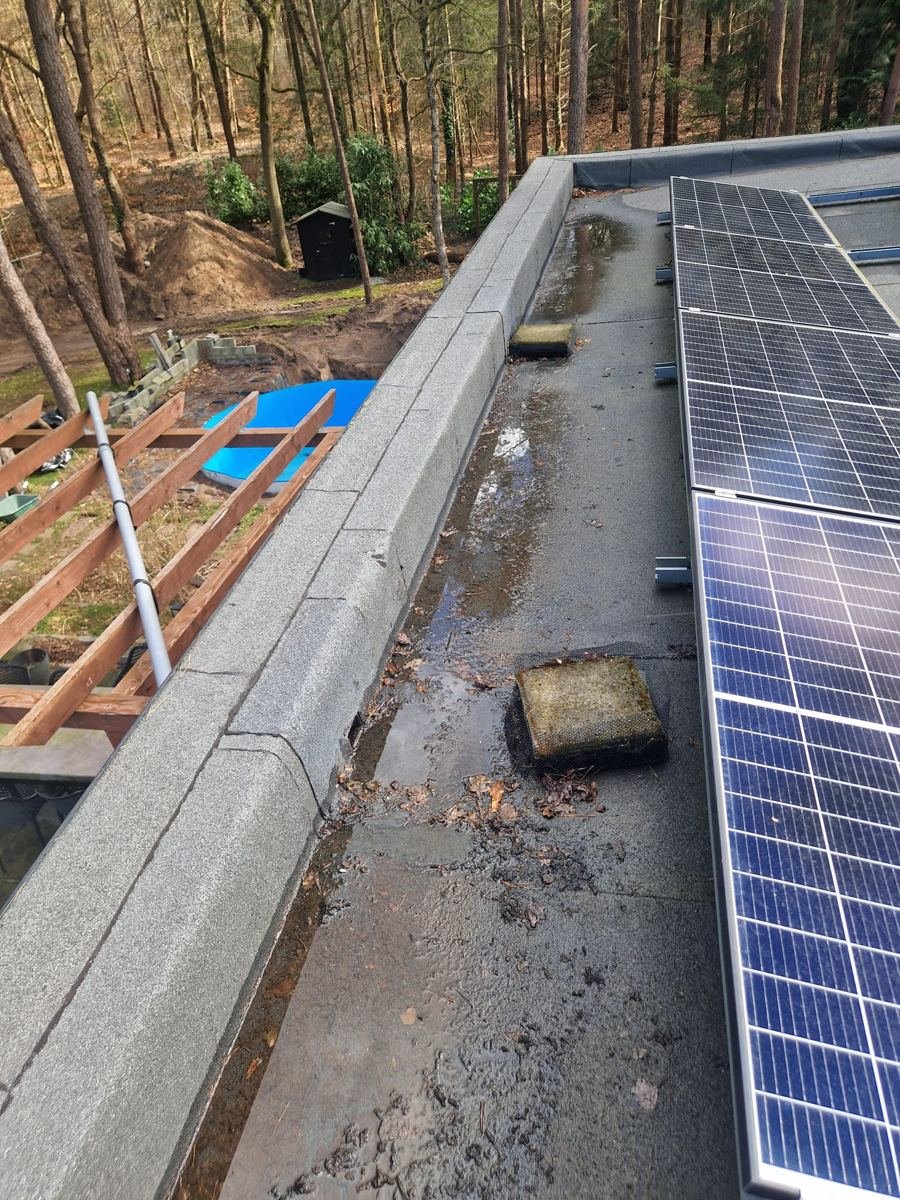 Plat dak met zonnepanelen en dakrand waar een lekkage wordt onderzocht